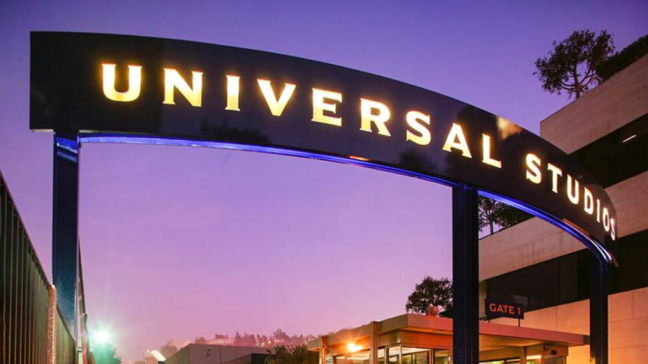 Illuminated "Universal Studios" sign. Buildings and sunset behind it.