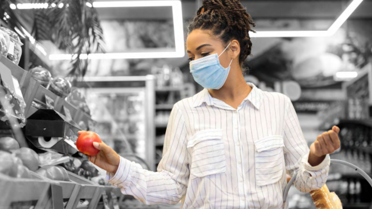 a person holds a red apple in a grocery store, a basket in their other hand