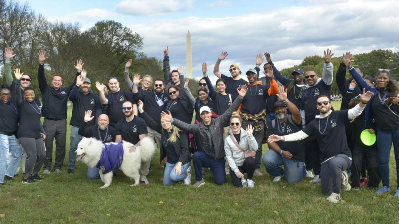 A group of people posed outside, smiling with raised hands. The Washington Monument in the distance.