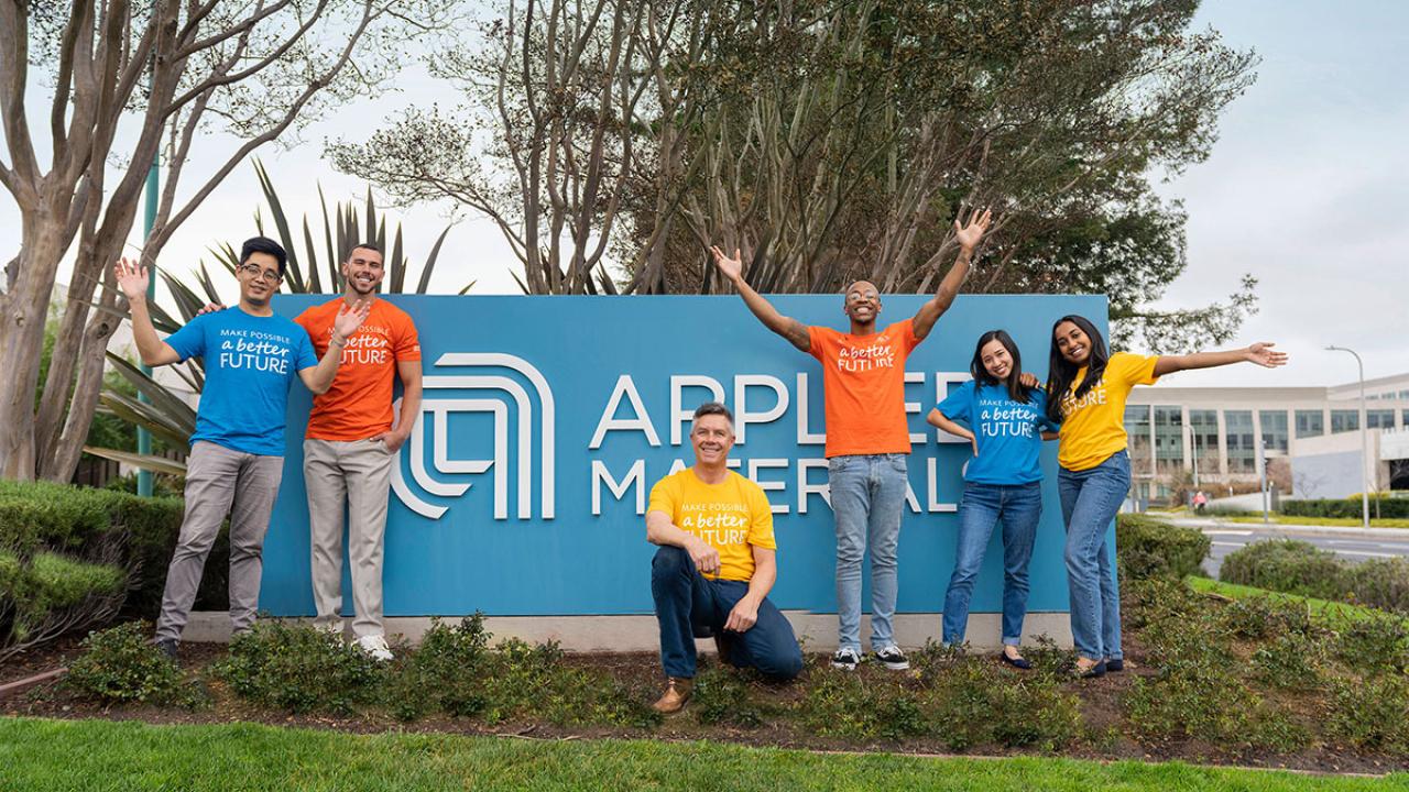 group smiling in front of Applied Materials logo