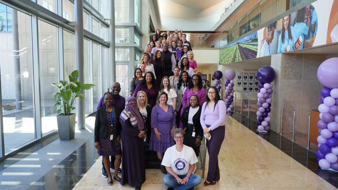 A group of people posed next to purple balloons and big windows