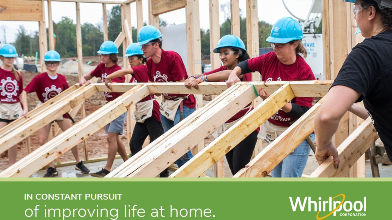 Volunteers lifting up framing for a house with text "In constant pursuit of improving life at home" with the Whirlpool logo