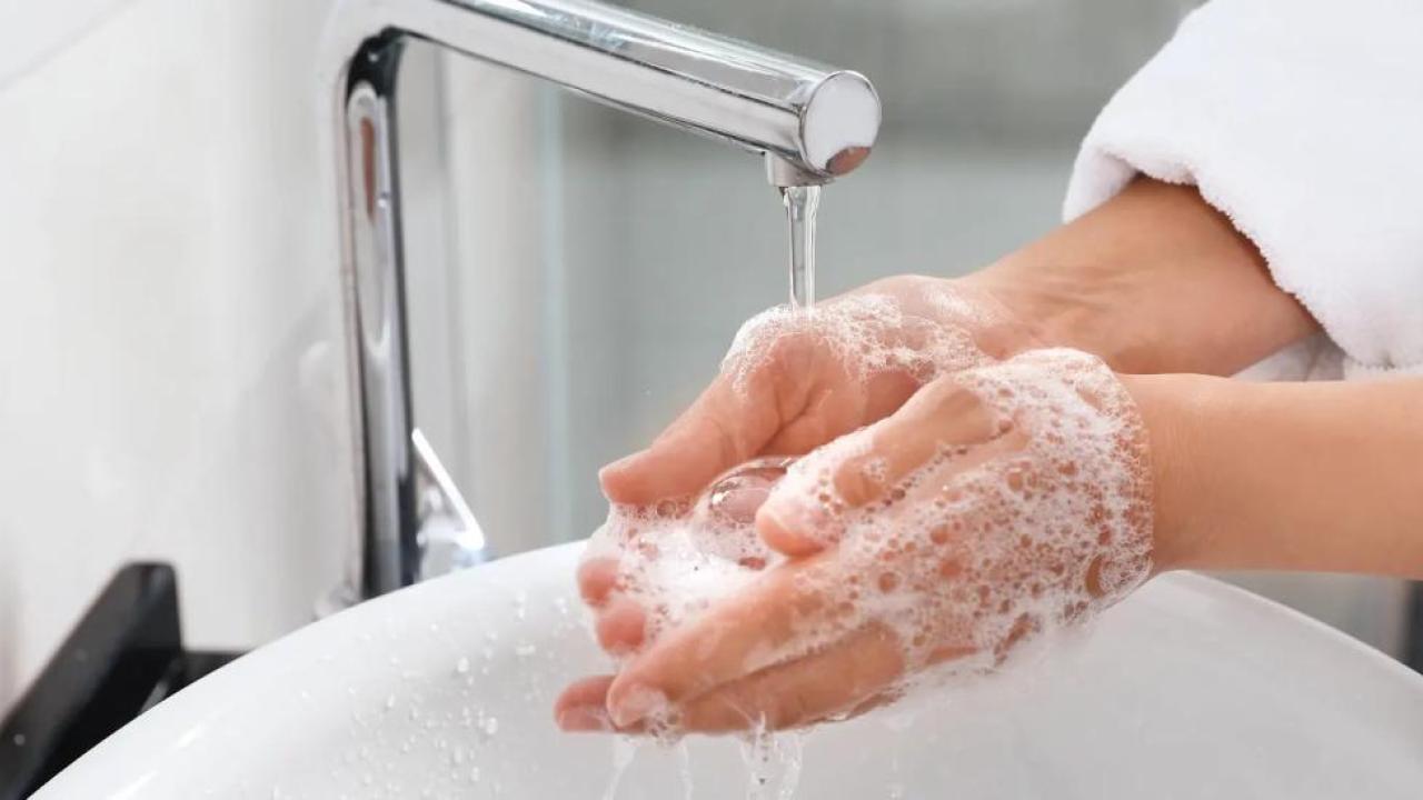 Close up of a person washing their hands in a sink.