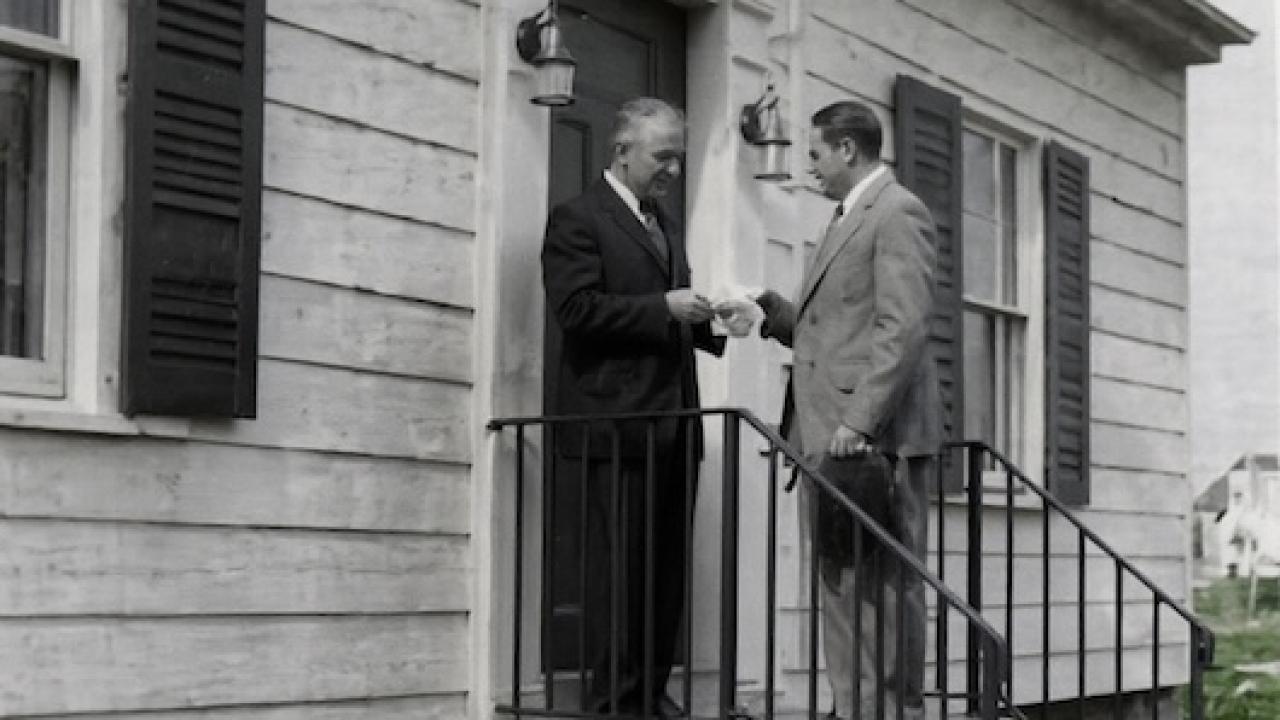 Webster Bank Founder Harold Webster Smith (pictured right with hat in hand) delivers the bank’s first loan to Joe Baltrush in December 1935 on the steps of his home at 114 Chambers Street in Waterbury.