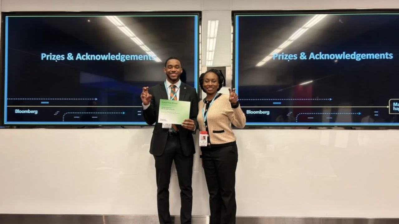 Two participants standing in front of digital displays, holding a certificate.