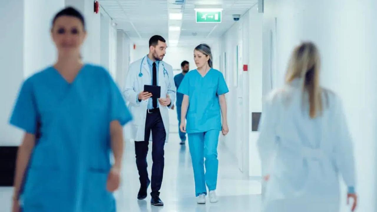 Medical professionals walking down a hallway. Two talking together.
