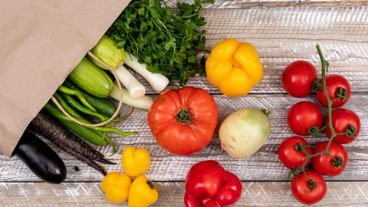 Vegetables shown spilling onto a table from a paper bag.