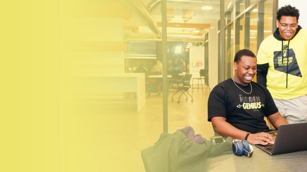 Two men on a laptop wearing "Hidden Genius" t-shirts