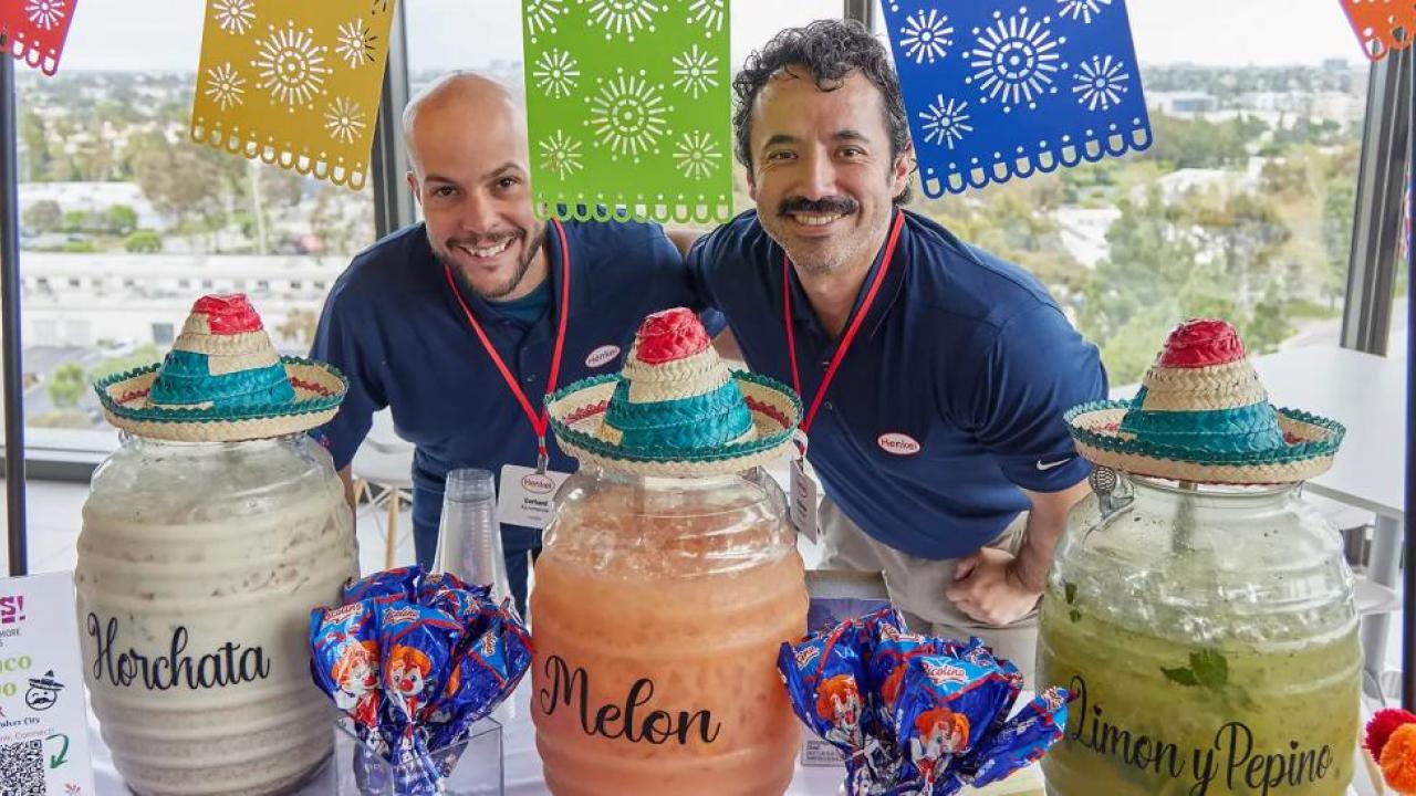 Two people smiling behind a table decorated and with three different drink dispenser