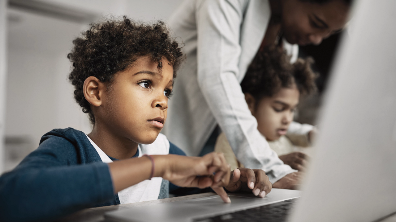 A child using a laptop next to another child on a laptop with an adult assisting them