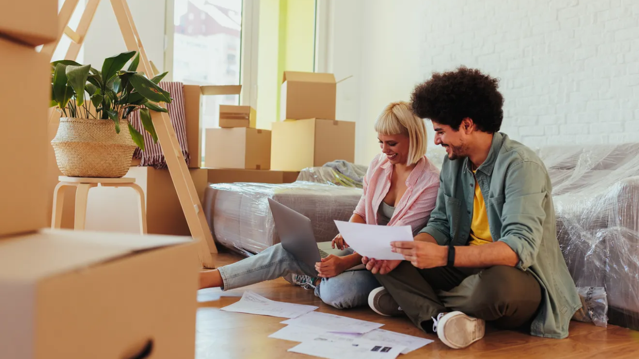 A couple sitting on the floor surrounded by moving boxes as they organize some paperwork