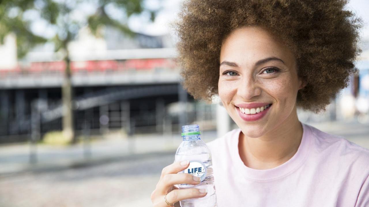 A smiling person holding a plastic bottle outside.