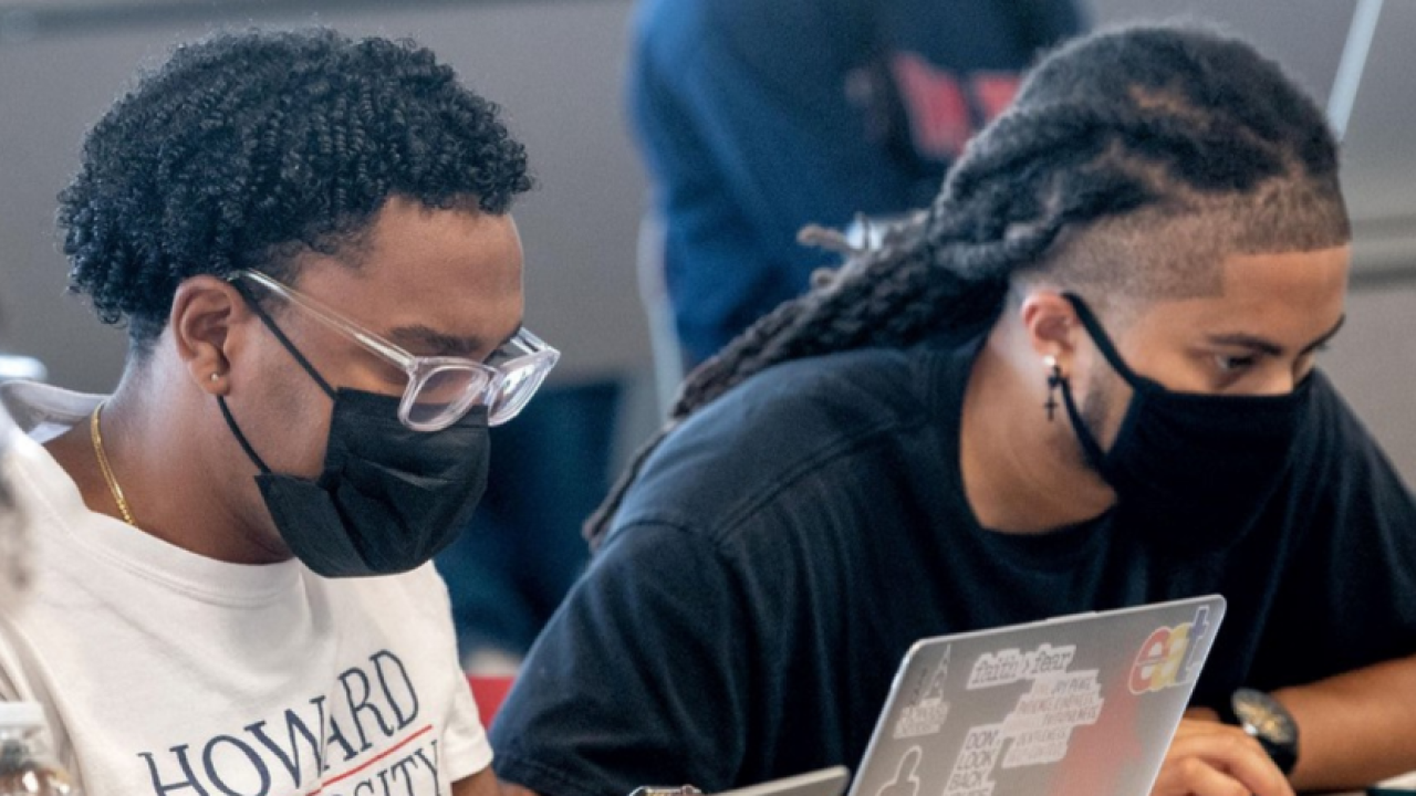 two Black Howard University students in masks work on laptops