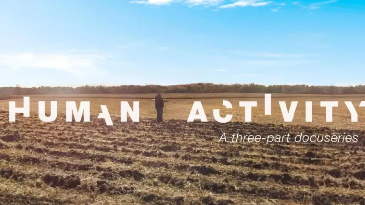 In white broken letters "Human activity". A person standing in a bare crop field, a blue sky above.