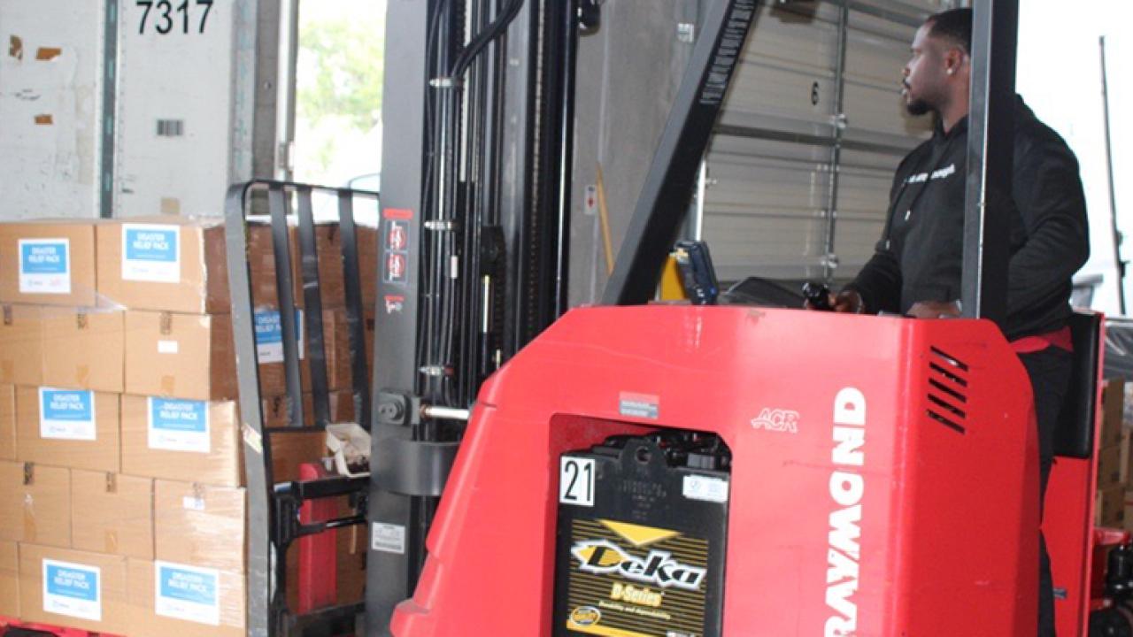 A person driving a forklift loaded with boxes.