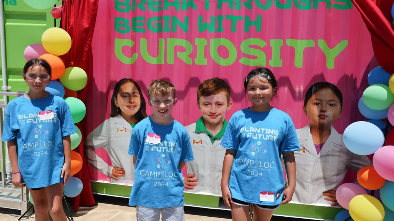 Three students next to their featured images in front of the Curiosity Cube.
