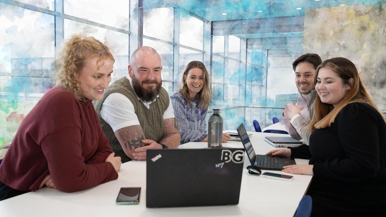 A group of seated people smiling at a laptop on a conference table.
