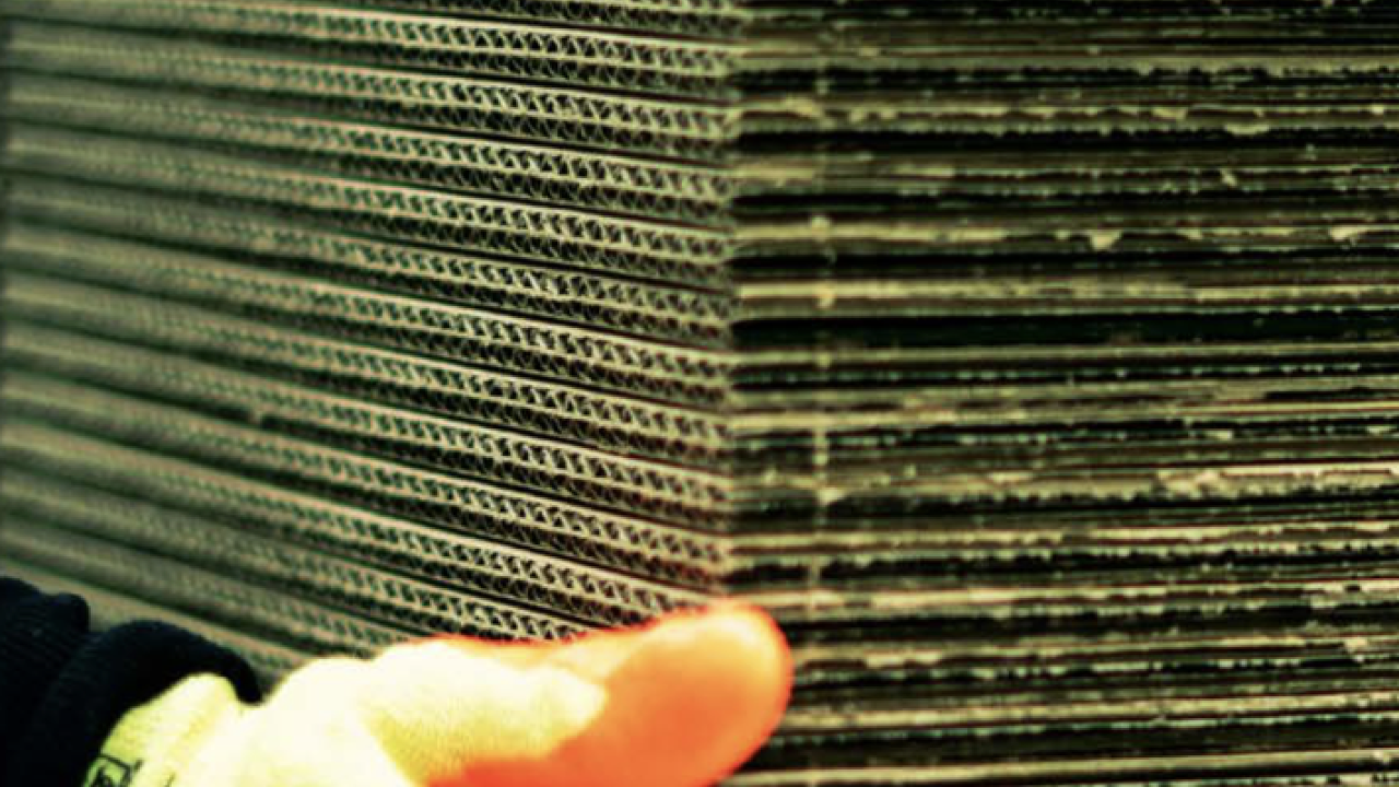 hand in an orange and yellow glove holding a stack of cardboard