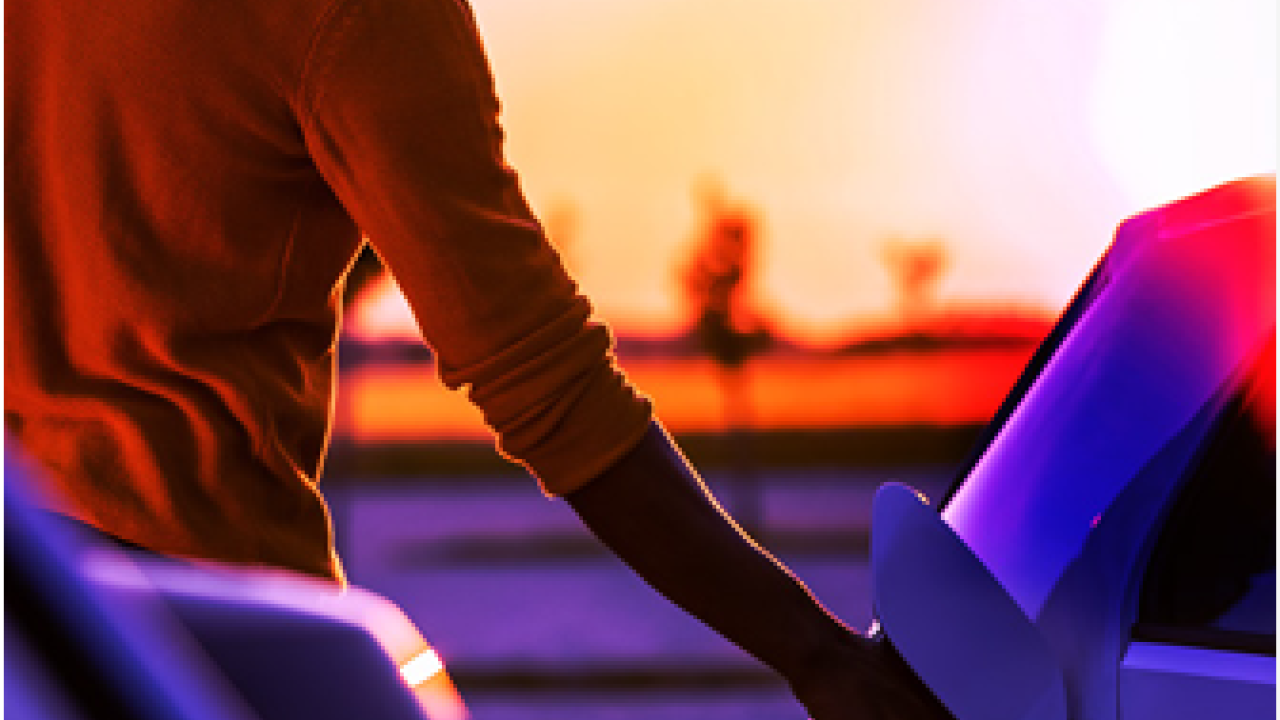 A person holding a plug to an electric vehicle port. A setting sun in the distance.