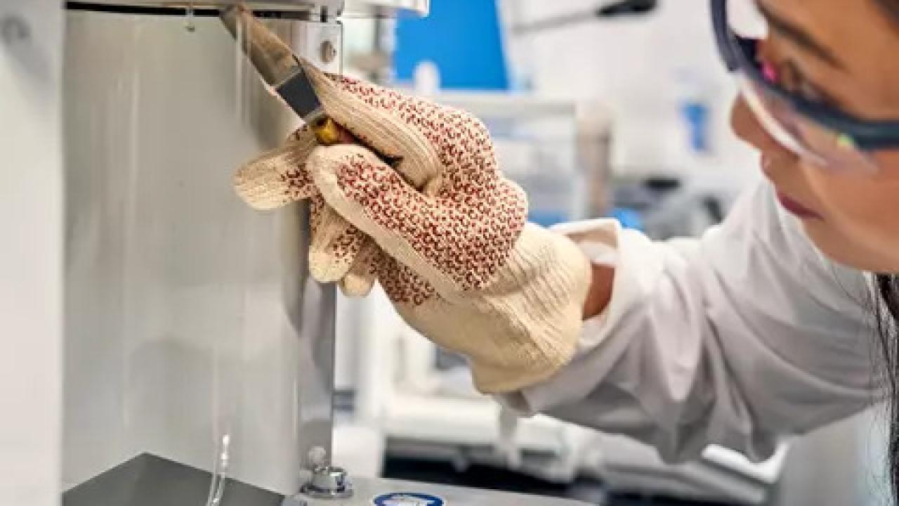 A person in protective lab wear using a scientific machine.