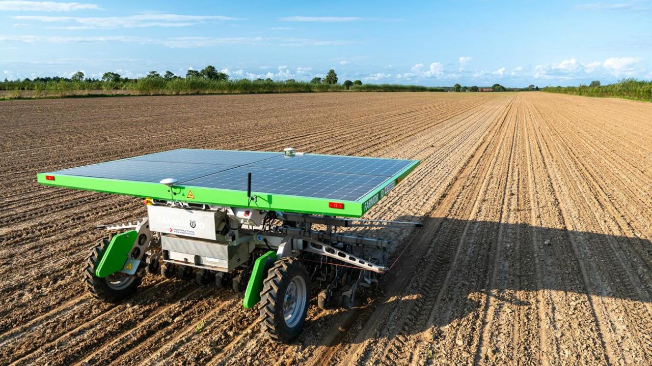 A solar panel on top of a small farm implement in a bare field. 