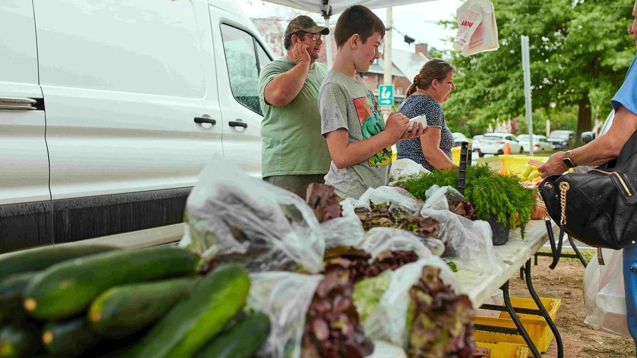 People under a tent behind tables with fresh vegetables on them