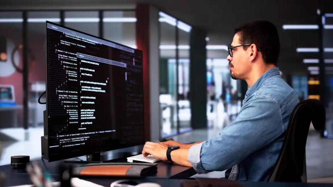 A person using a keyboard, looking at a large digital screen in a dark office setting.