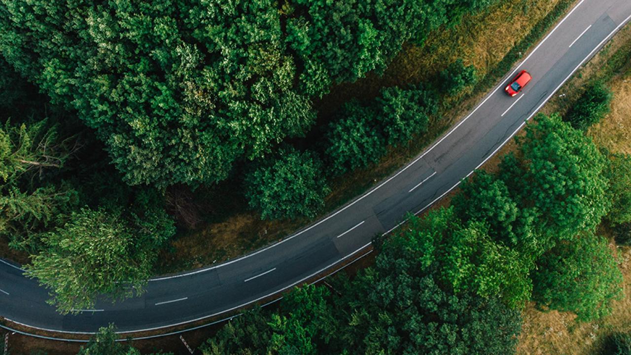 Aerial view of a single red car on a two-way road through forested area