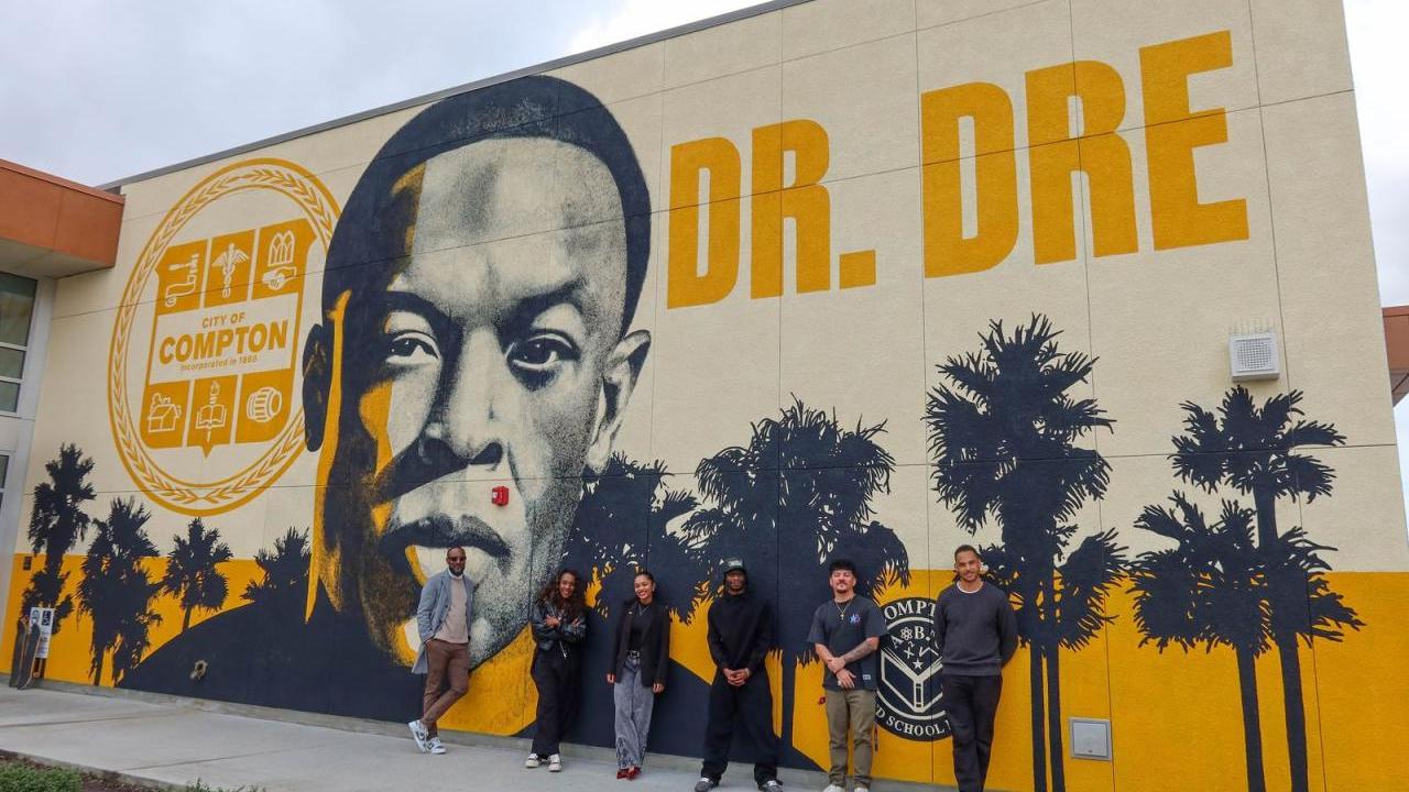 AEG team members pose outside Compton High School in front of the Andre “Dr. Dre” Young Performing Arts Center mural during a campus visit focused on career exposure and community engagement.