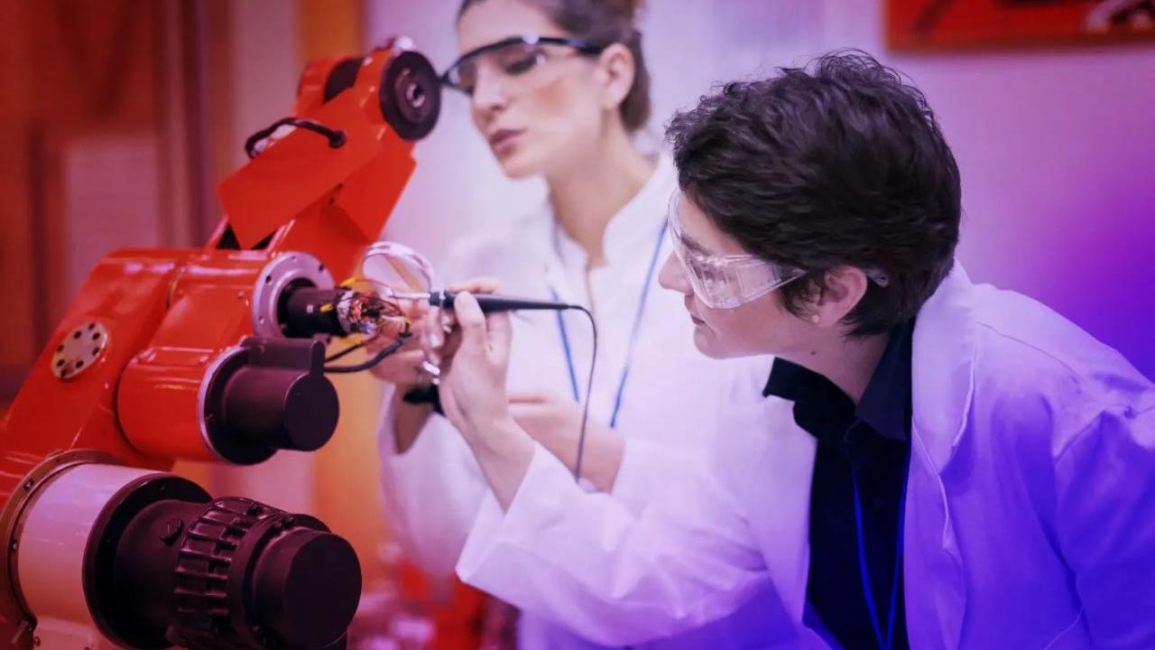 women in lab coats working on a piece of robotic equipment