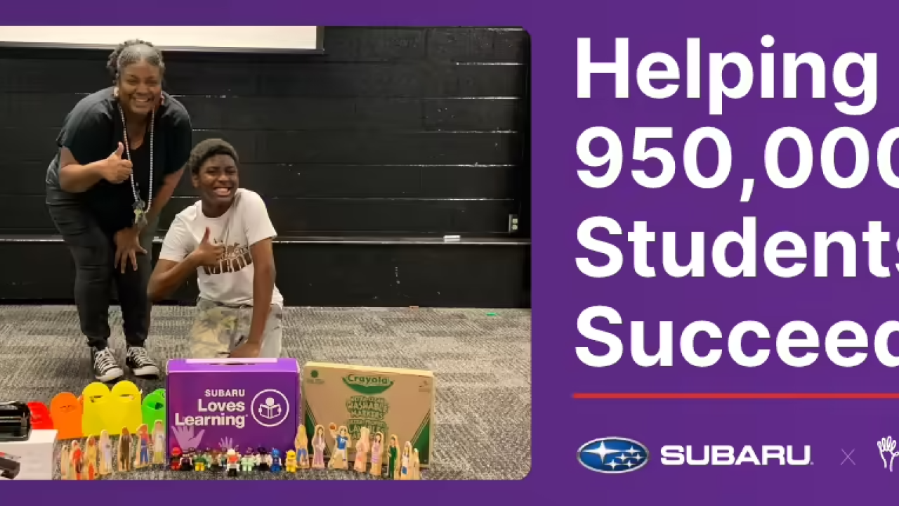 A student and an adult behind school supplies, giving thumbs up