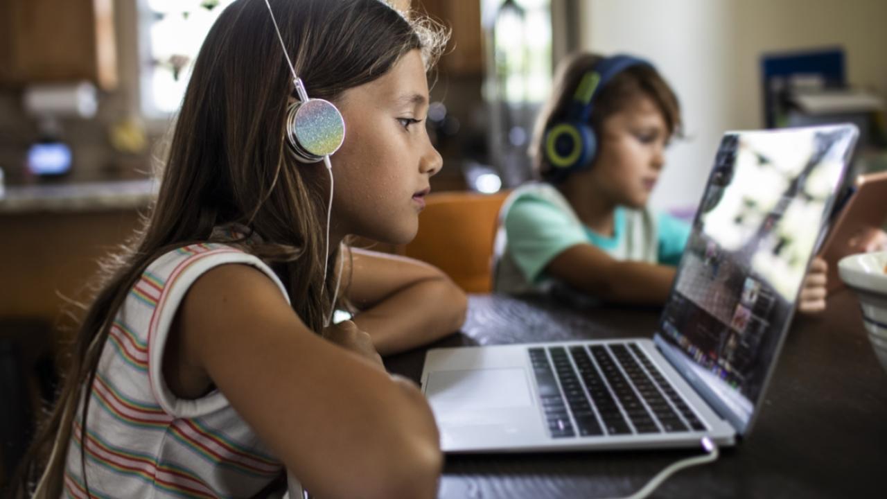 two kids wearing headphones, each on a laptop in a kitchen setting