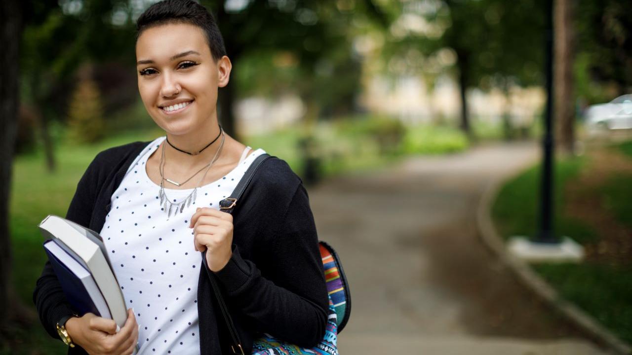 A smiling person with backpack and books.