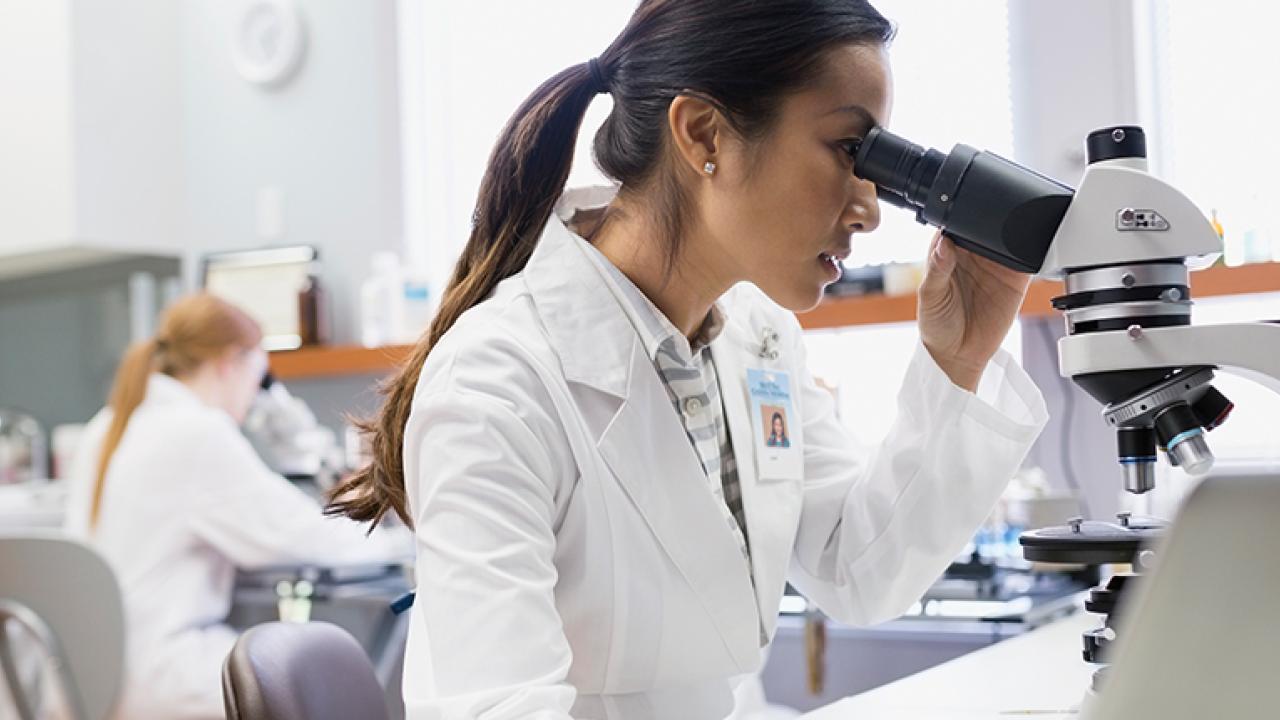 A person in white lab coat looking in a microscope