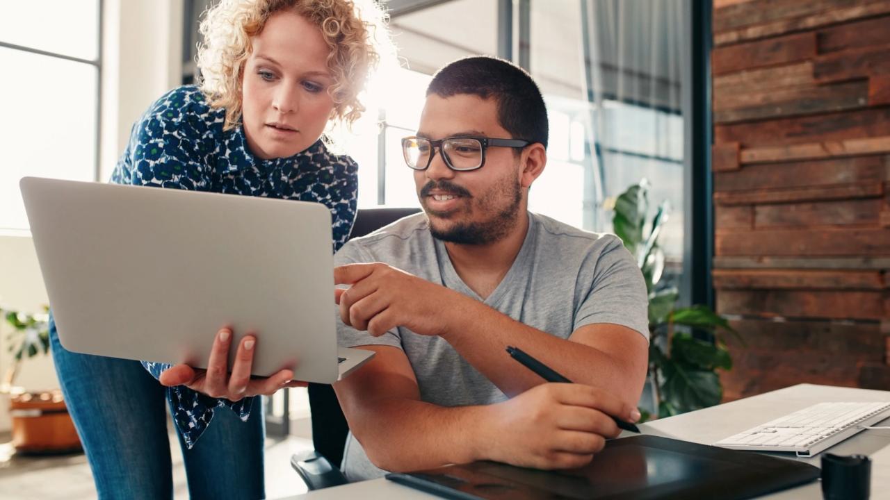 Two people looking at the same laptop in an office setting