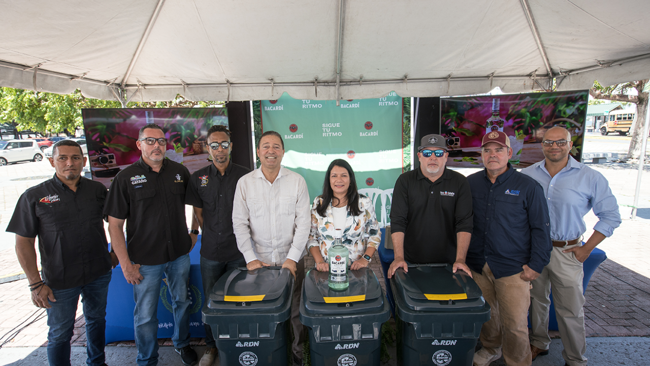 8 people standing together under a tent with 3 recycling bins