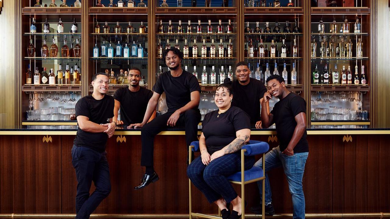 A group of students in black t-shirts posed in front of a bar