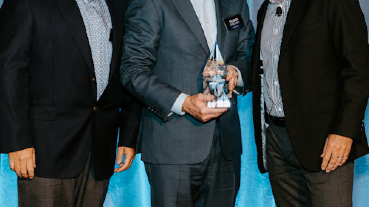Three people stood next to each other holding an award, in front of a blue backdrop  