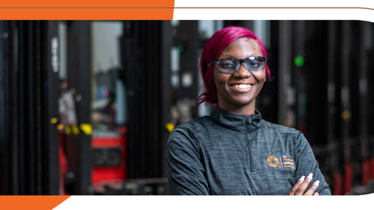 A smiling person with arms crossed in front of a row of machines.
