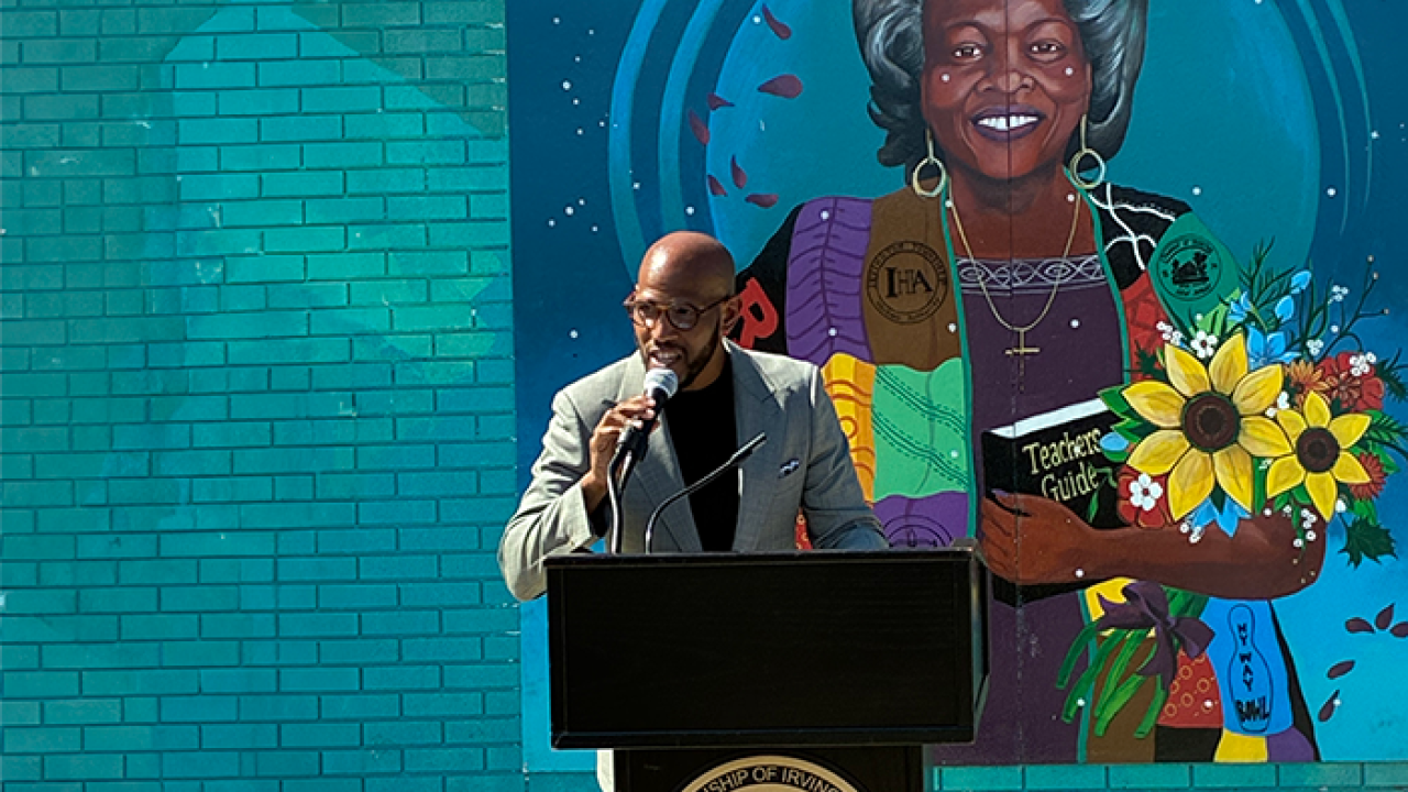 Someone speaking at a podium in front of a large mural