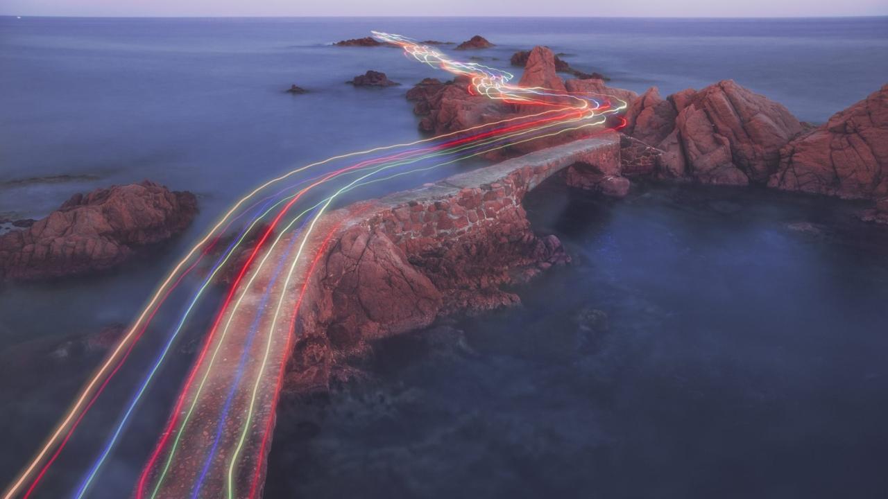 streams of colorful light across a narrow land bridge over an expanse of water