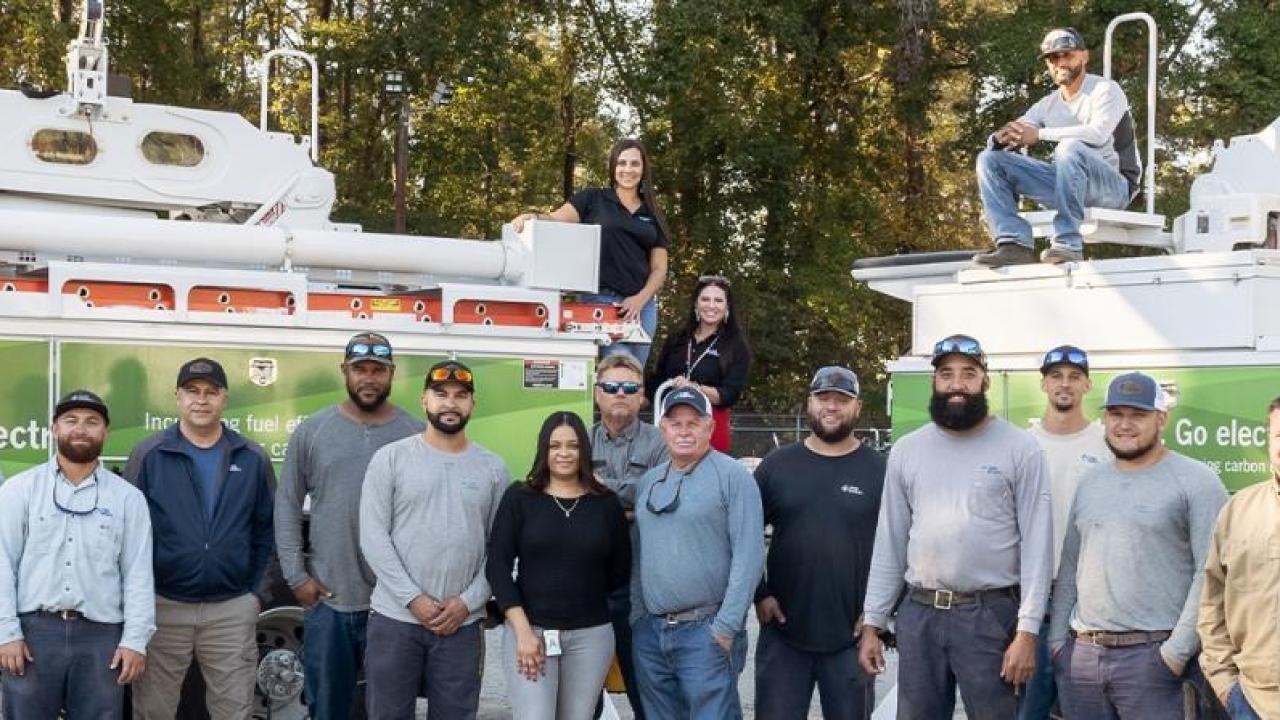 A large group of employees posed in front of two large trucks with extension buckets.