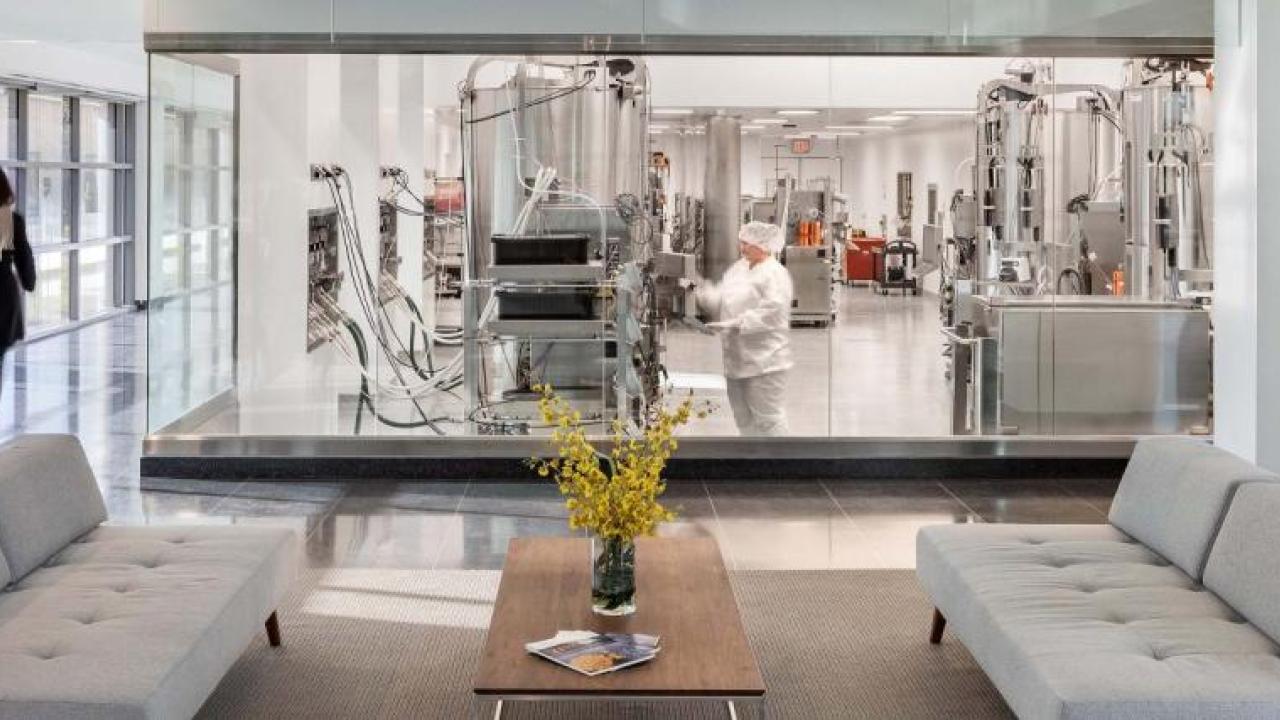 An office building with clear window-walls surrounding a lab with large equipment.