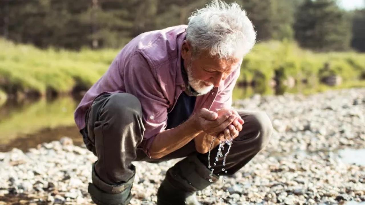 A person crouched down at the side of a river 