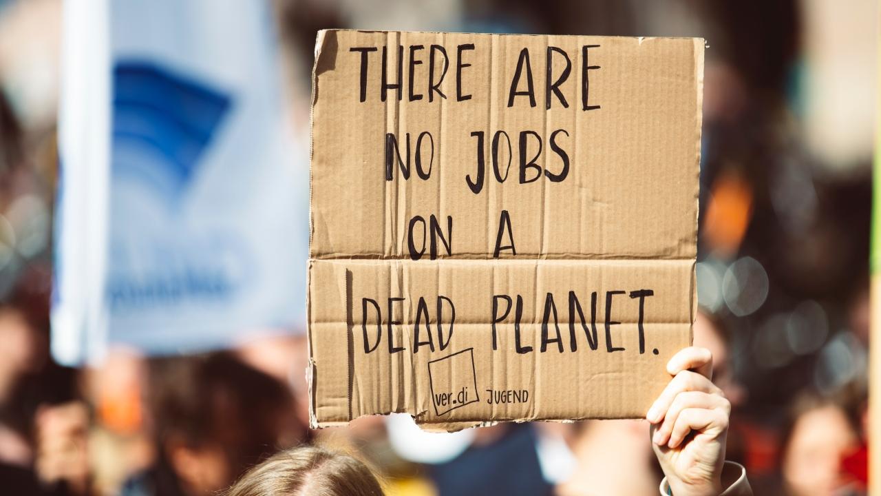 Protester with a cardboard sign reading "THERE ARE NO JOBS ON A DEAD PLANET"