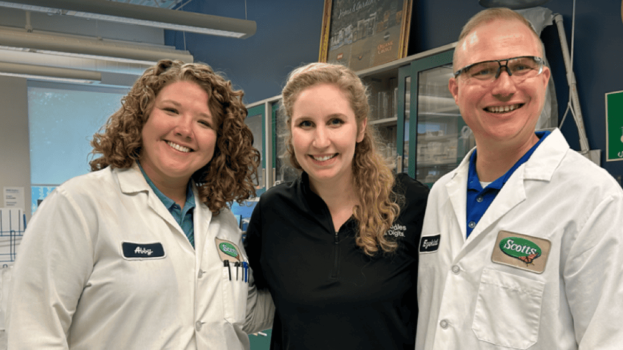 Three people posed together, two in lab protective wear.