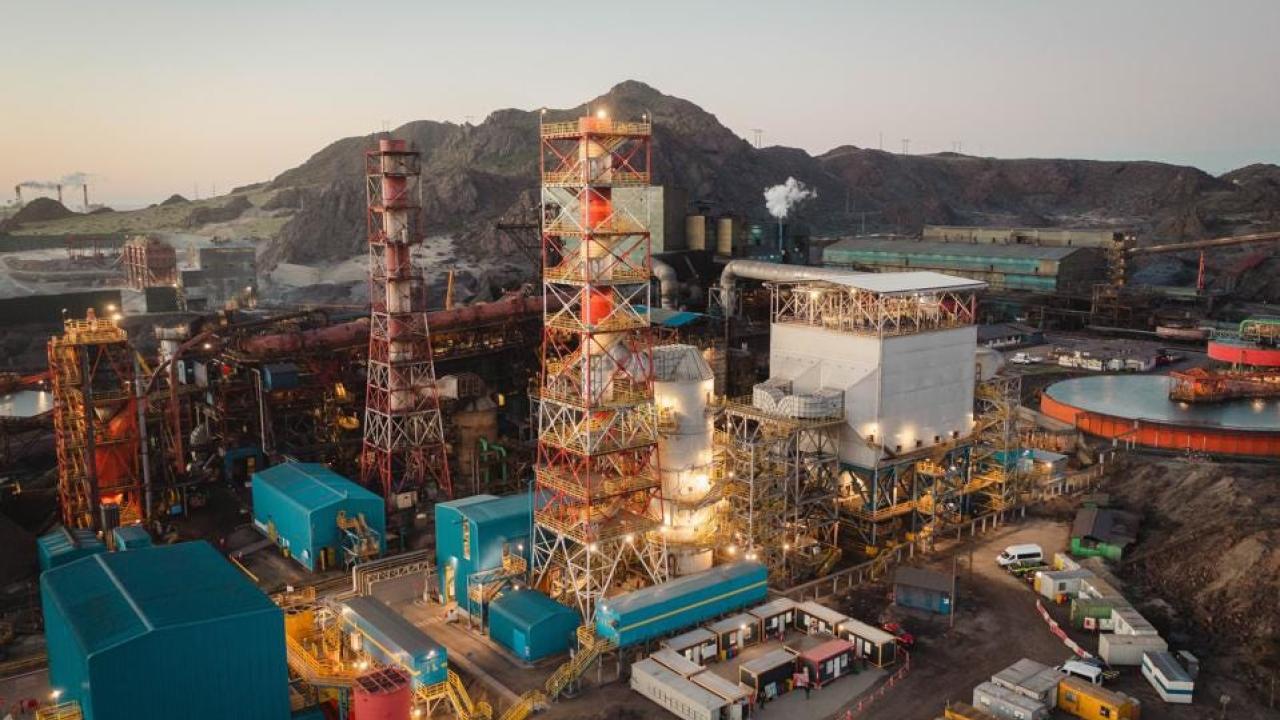 aerial view of a large industrial complex, a mountain range in the background.