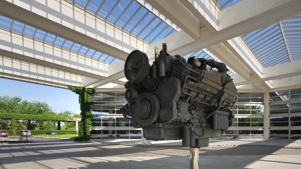 a large model motor on a stand in a cement walkway under glass and beam roof at Cumming headquarters