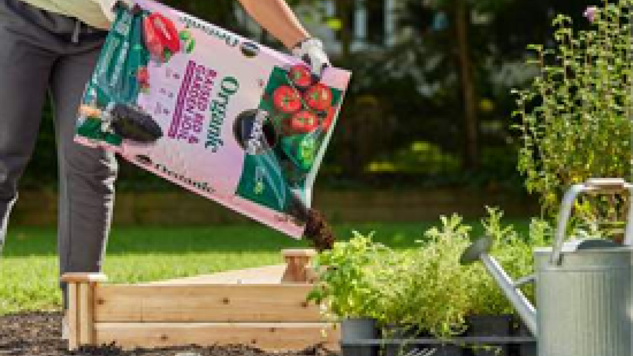 A person pouring soil from a bag into a raised garden bed outside.