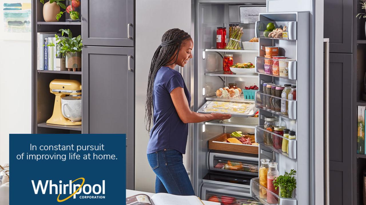 a person holding a pan of food in an open fridge. Whirlpool logo and "In constant pursuit of improving life at home" in the right lower corner.